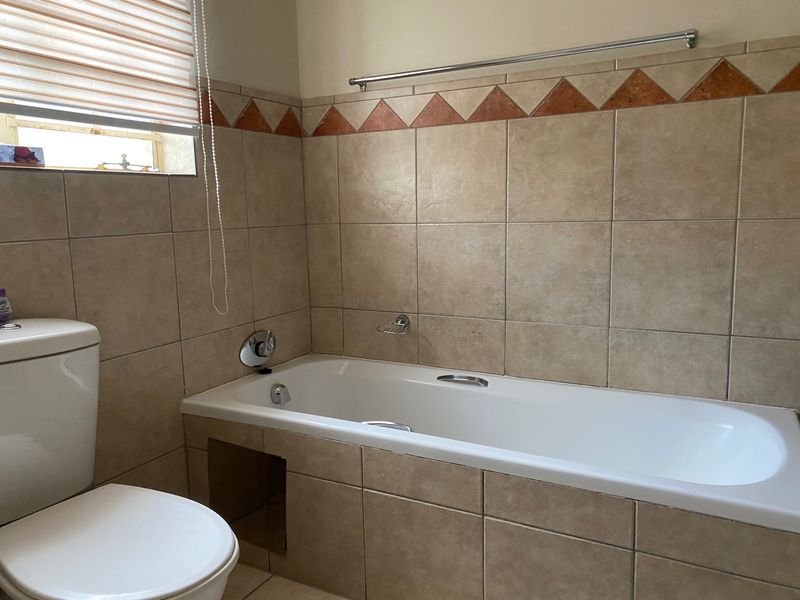 A functional bathroom featuring a built-in bathtub with tiled surround, a toilet, and decorative border tiles.