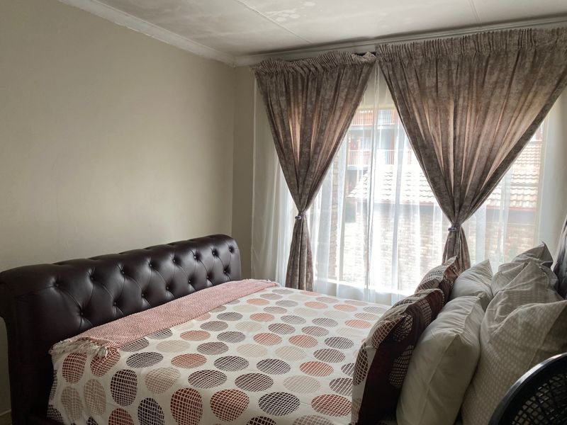 A bedroom featuring neutral walls and natural light through window curtains, showing signs of ceiling water damage.