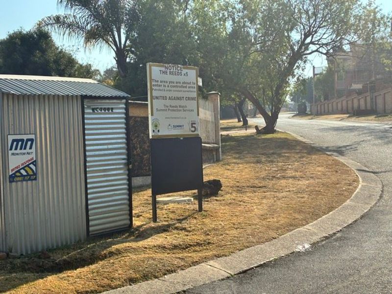A street-level view of the neighbourhood approach featuring a security notice board and a small utility structure on the roadside.