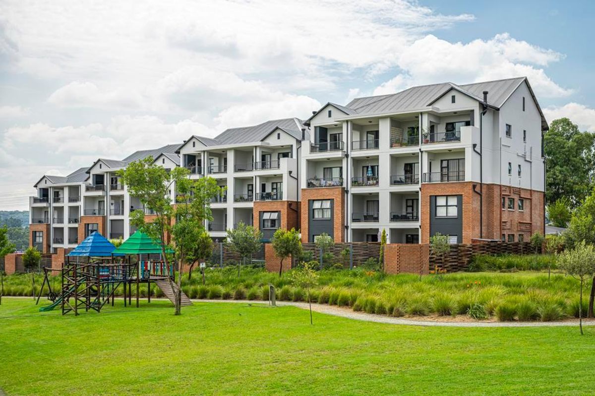 A view of the apartment complex rear elevation featuring multi-level balconies, brick and plaster finishes, and a well-maintained communal garden area.