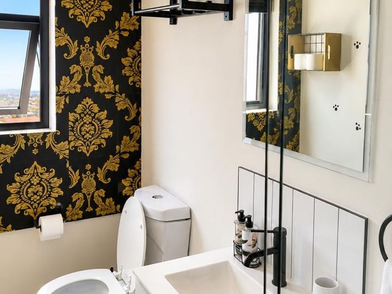 A modern bathroom featuring a vanity with basin, toilet, shower screen, and decorative wallpaper, offering a clean and well-maintained aesthetic.