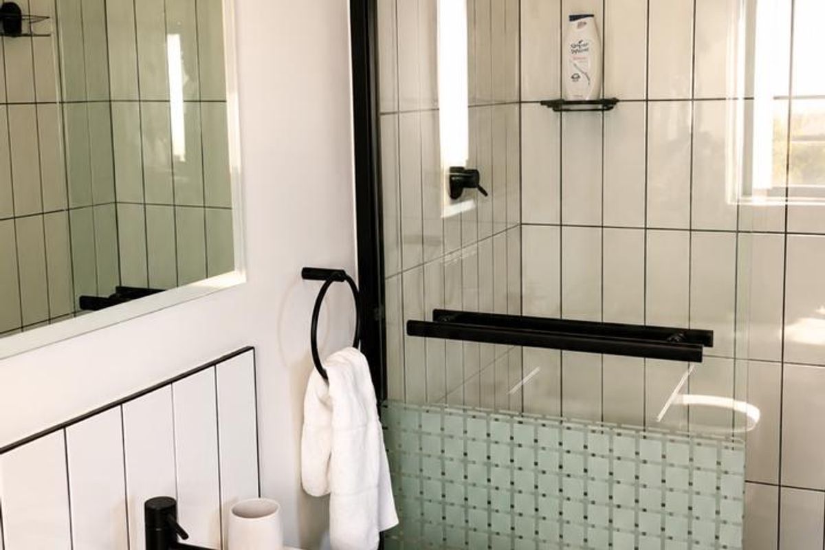 Modern bathroom featuring a sleek vanity with black fixtures, a glass-enclosed shower with subway tiling, and a decorative mosaic accent wall.