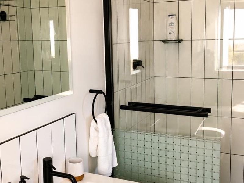 Modern bathroom featuring a sleek vanity with black fixtures, a glass-enclosed shower with subway tiling, and a decorative mosaic accent wall.