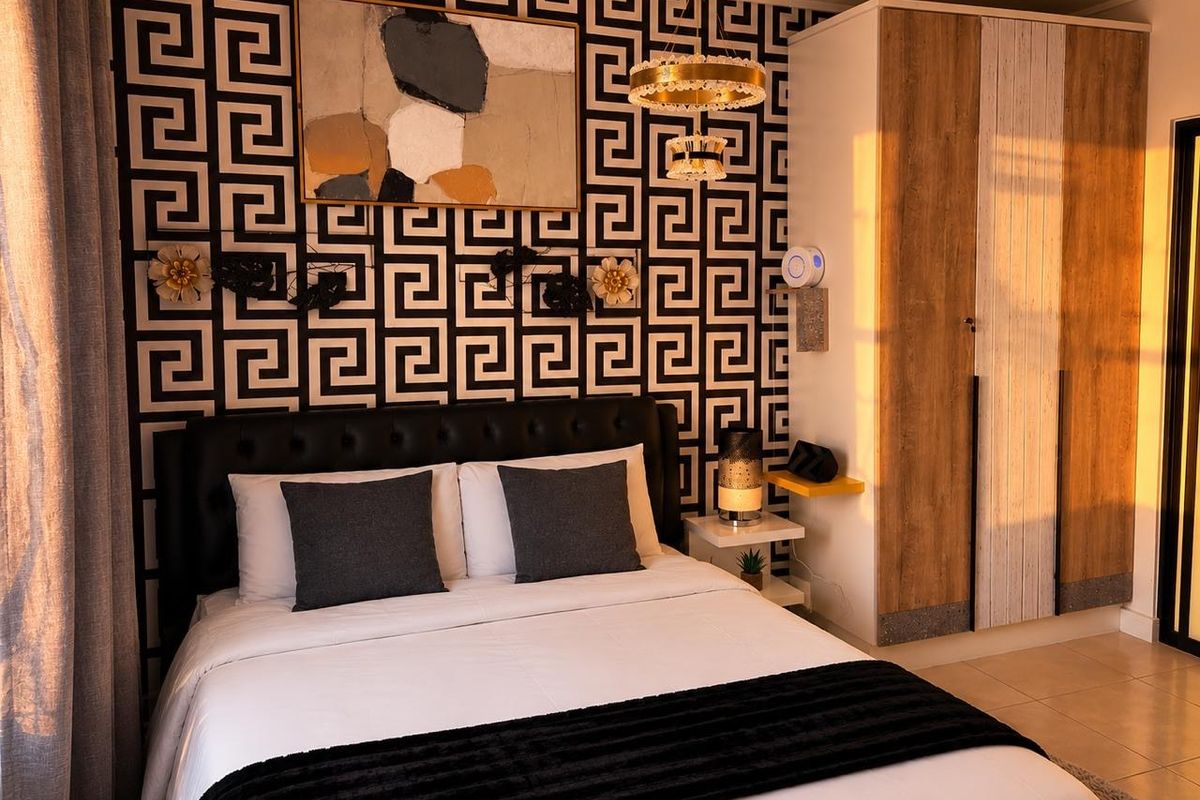 A well-lit bedroom featuring a built-in wardrobe, tiled flooring, and a decorative feature wall with a modern pendant light fixture.
