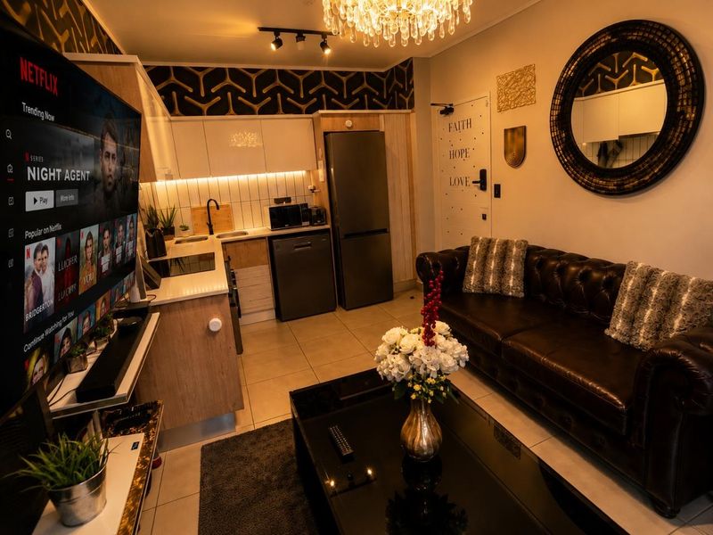 A modern open-plan living area featuring a compact kitchen with built-in cabinetry, tiled flooring, and stylish lighting fixtures, creating a functional and inviting space.