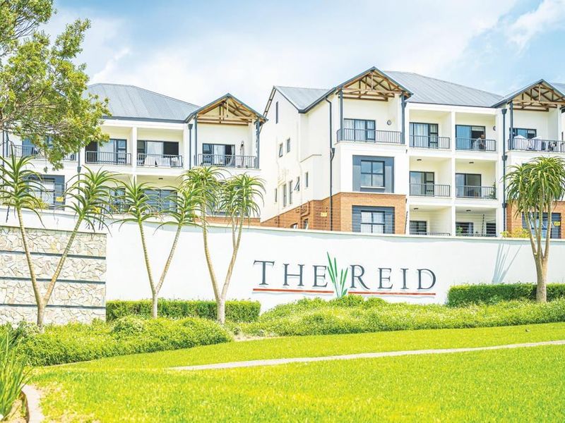 Exterior view of The Reid apartment complex featuring modern multi-story residential buildings, landscaped gardens, and a prominent perimeter wall.