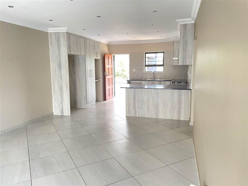 Spacious open-plan living area featuring a modern kitchen with built-in cabinetry, a breakfast island, and neutral tiled flooring throughout.