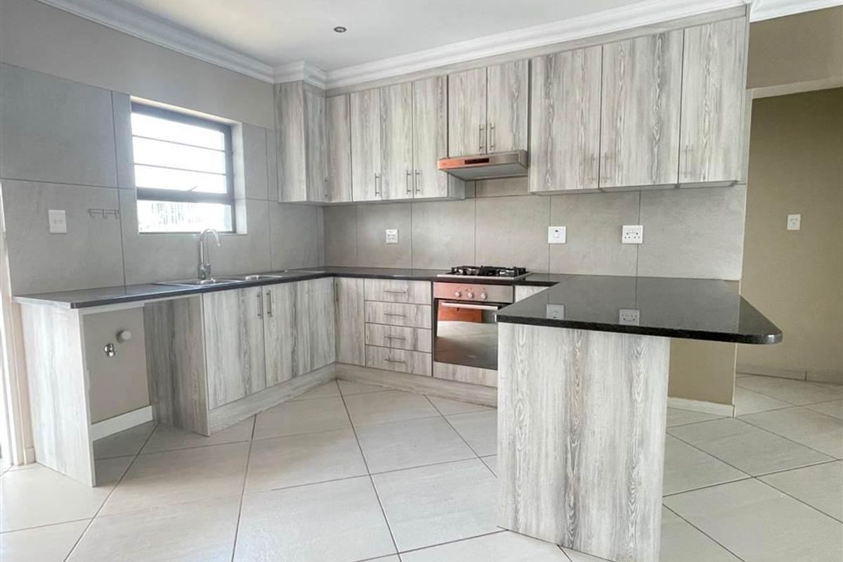Modern kitchen featuring light wood-grain cabinetry, granite countertops, built-in oven, gas hob, extractor fan, and tiled flooring.