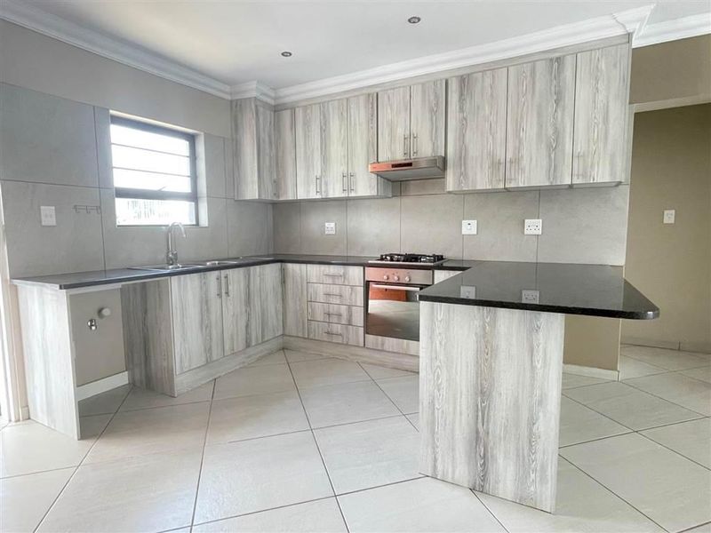 Modern kitchen featuring light wood-grain cabinetry, granite countertops, built-in oven, gas hob, extractor fan, and tiled flooring.