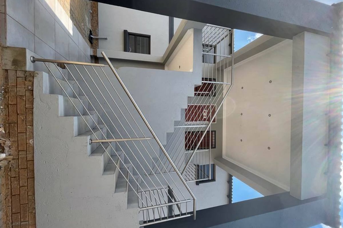 A modern exterior view of an apartment building featuring a concrete staircase with stainless steel balustrades and a covered patio area.