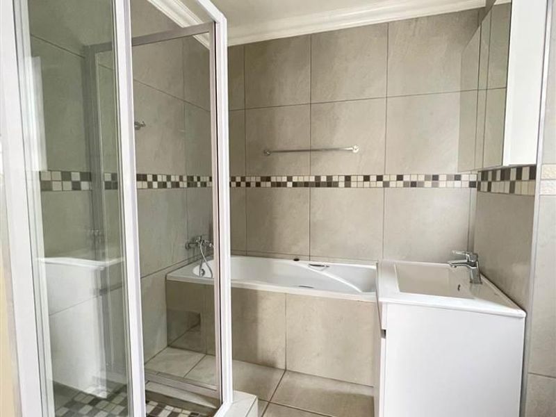 A clean, modern bathroom featuring a glass-enclosed shower, a built-in bathtub, and a vanity basin with neutral wall and floor tiling.