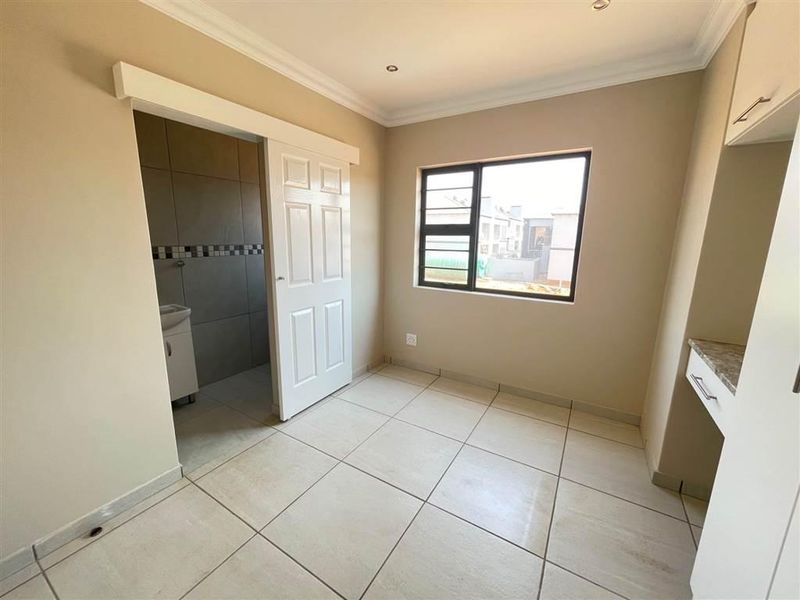 A bright, empty bedroom featuring tiled flooring, a built-in vanity, and a sliding door leading to an en-suite bathroom.