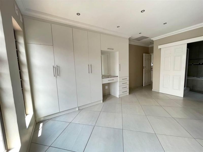 Spacious bedroom featuring extensive built-in cupboards with an integrated vanity station, neutral tiled flooring, and recessed lighting.