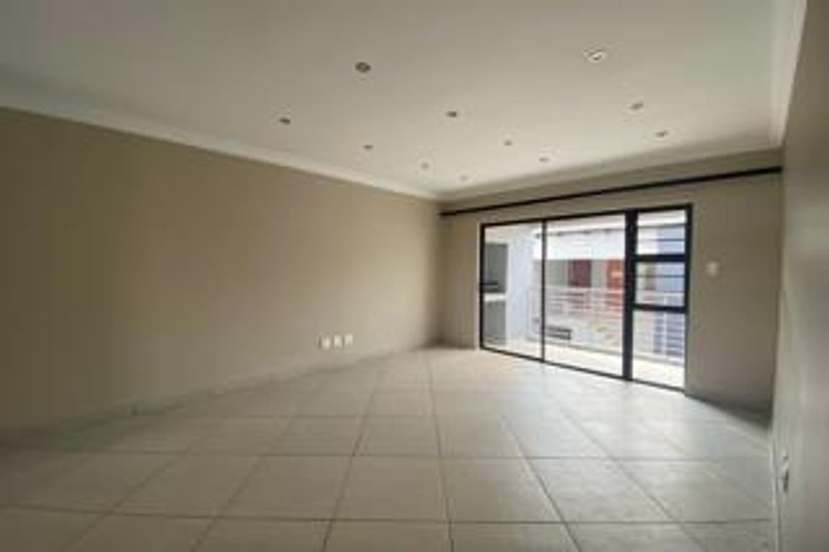 Spacious, empty living area featuring neutral tiled flooring, recessed downlighting, and a large sliding glass door providing access to an outdoor balcony.