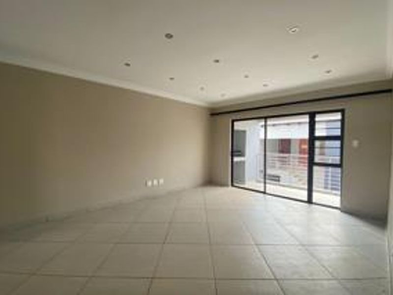 Spacious, empty living area featuring neutral tiled flooring, recessed downlighting, and a large sliding glass door providing access to an outdoor balcony.