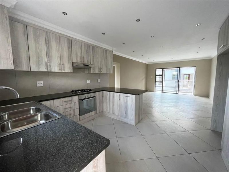 Spacious open-plan kitchen and living area featuring modern wood-finish cabinetry, granite countertops, built-in appliances, and large sliding doors leading to a balcony.