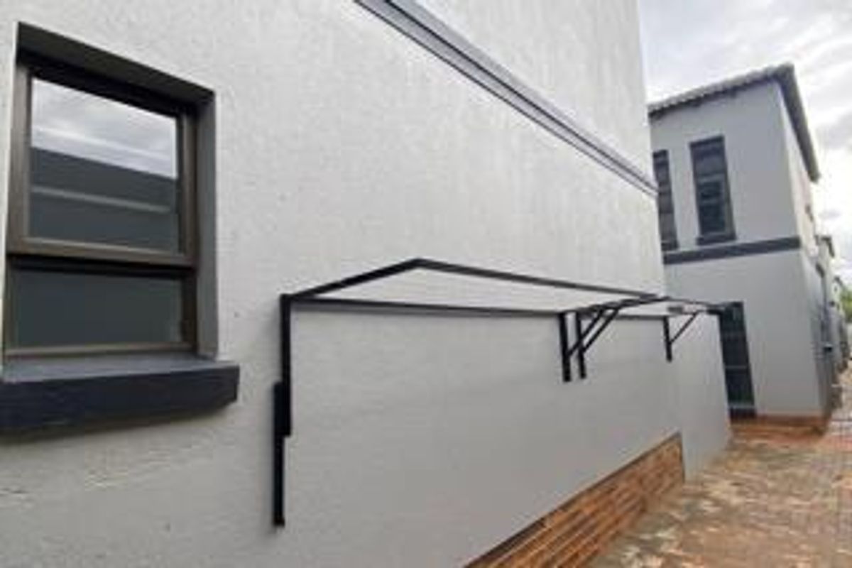 A view of the rear exterior of the apartment building featuring a paved walkway, aluminium window frames, and a fixed metal washing line frame.