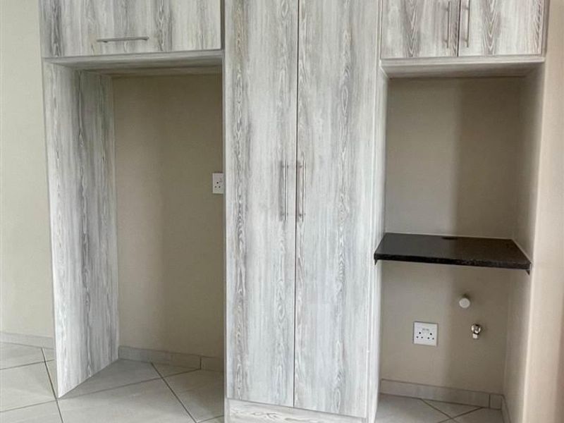 A clean kitchen area featuring light wood-grain built-in cabinetry, tiled flooring, and dedicated spaces for appliances with integrated plumbing and electrical points.