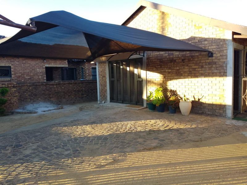Front exterior view of a face brick house featuring a shade sail covering a cobblestone paved driveway and entrance area.