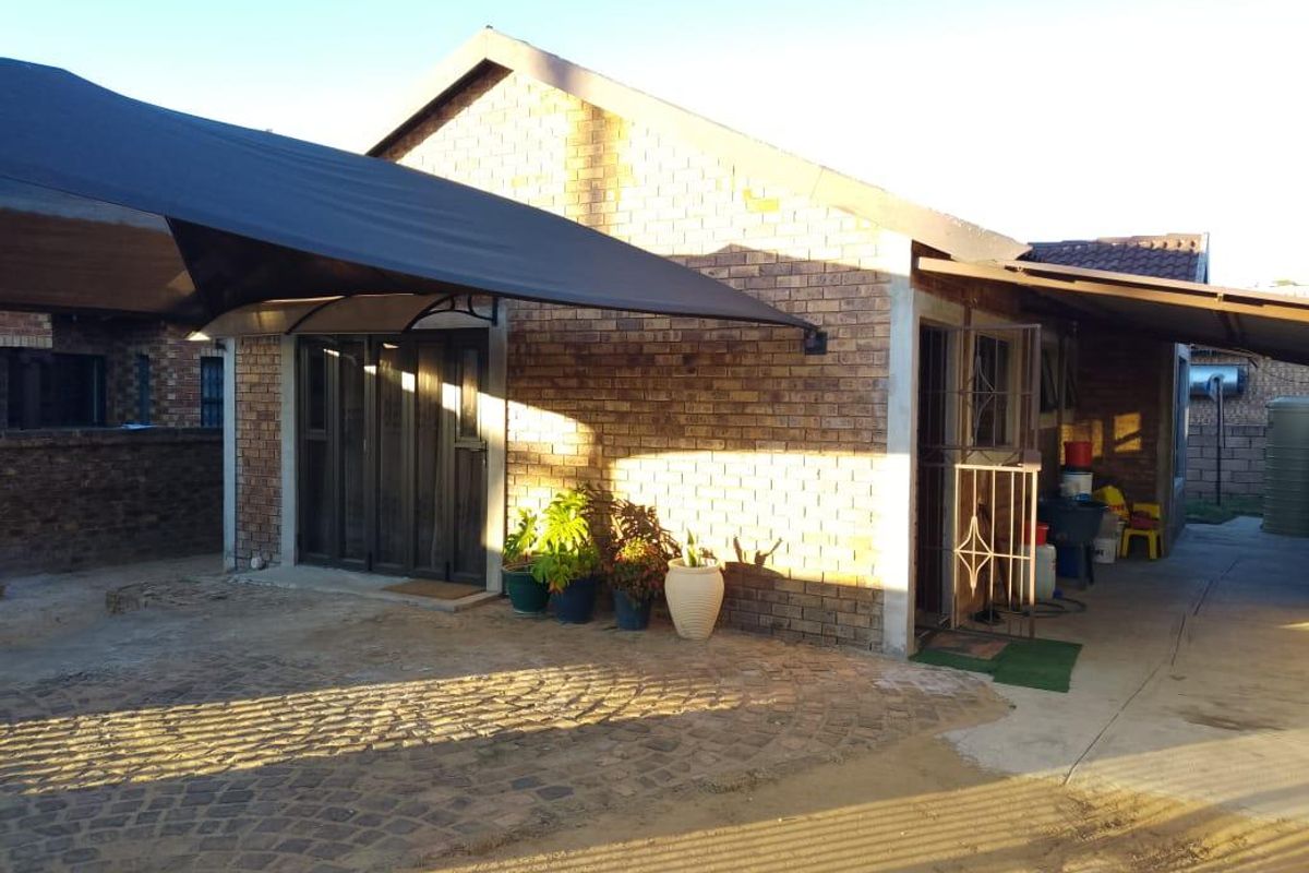 Rear exterior view of the property featuring face brick walls, a covered patio area with a shade sail, and paved outdoor space.