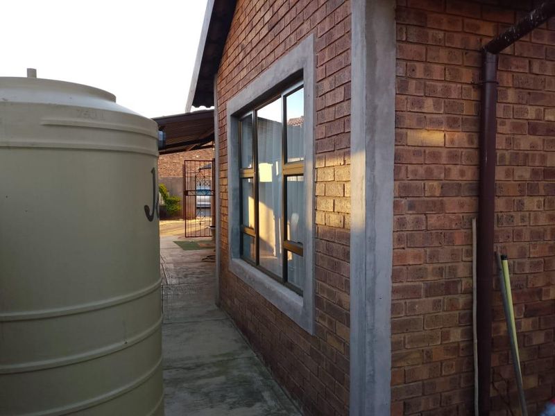 Side view of the property showing face brick exterior, aluminium window frames, and a water storage tank on a concrete pathway.