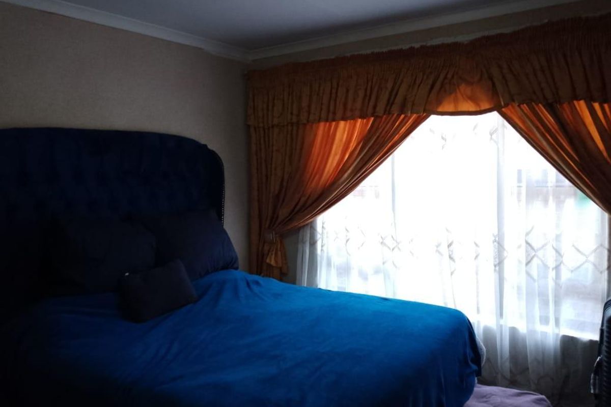 A bedroom featuring a large window with draped curtains, providing natural light to the space.