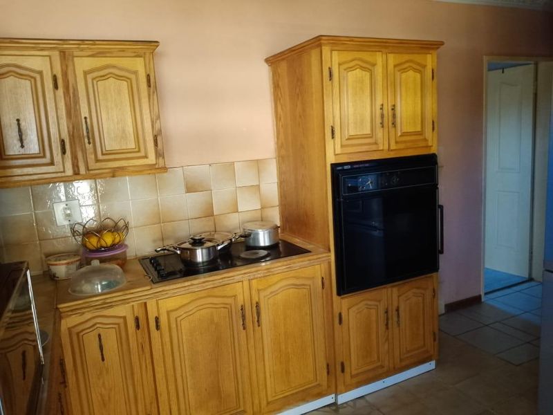 A functional kitchen featuring traditional wooden cabinetry, a built-in oven, an electric hob, and tiled splashbacks, offering a classic layout with potential for modernization.