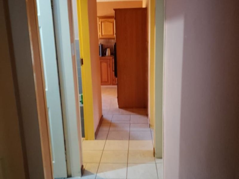 A narrow residential hallway featuring tiled flooring and access to multiple rooms, leading towards a kitchen area in the background.