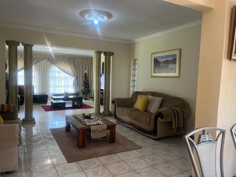 Spacious open-plan living area featuring decorative columns, ceramic floor tiles, and a glass block accent wall, creating a connected and versatile living space.