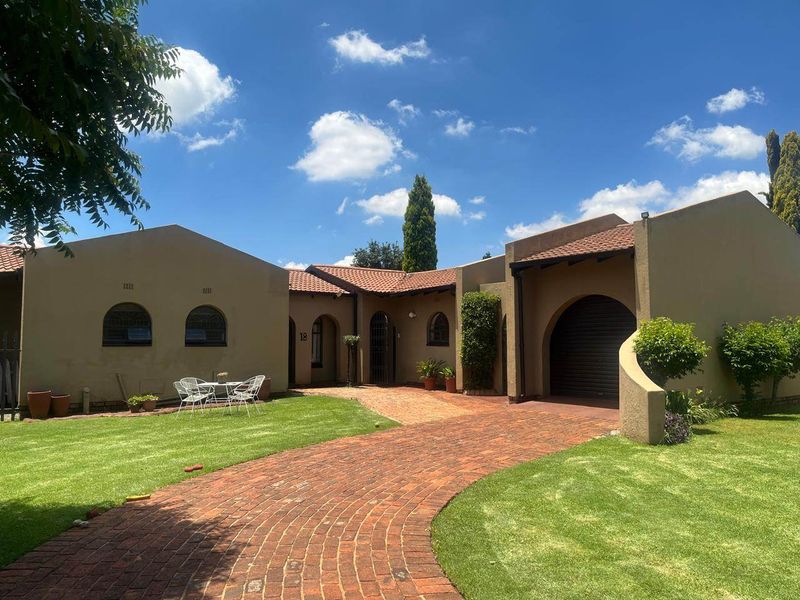 Front elevation of a single-story house featuring a brick driveway, arched garage entrance, and well-maintained lawn.