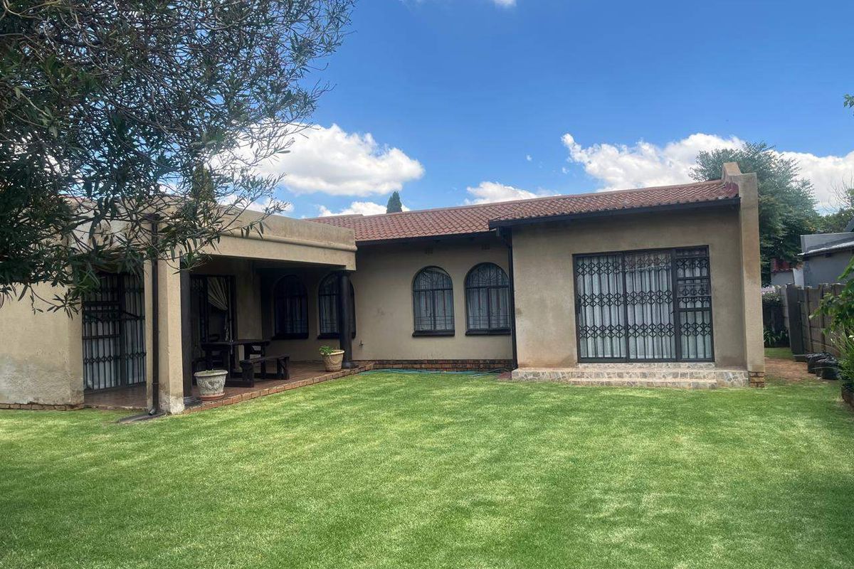 Rear view of the house featuring a covered patio, arched windows, sliding glass doors with security gates, and a well-maintained lawn.
