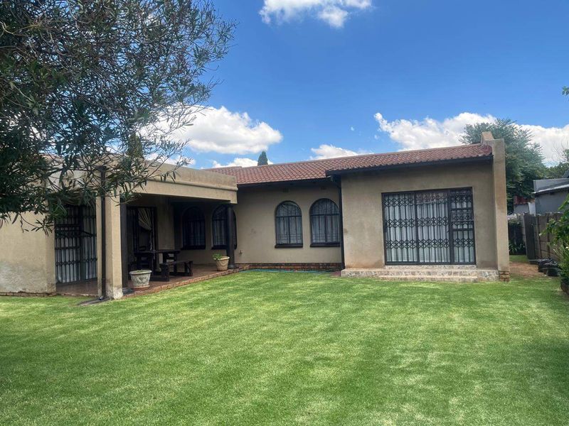Rear view of the house featuring a covered patio, arched windows, sliding glass doors with security gates, and a well-maintained lawn.