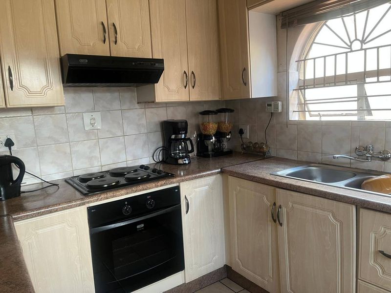 A functional kitchen featuring light wood-finish cabinetry, laminate countertops, a built-in oven with electric hob, and a classic arched window.