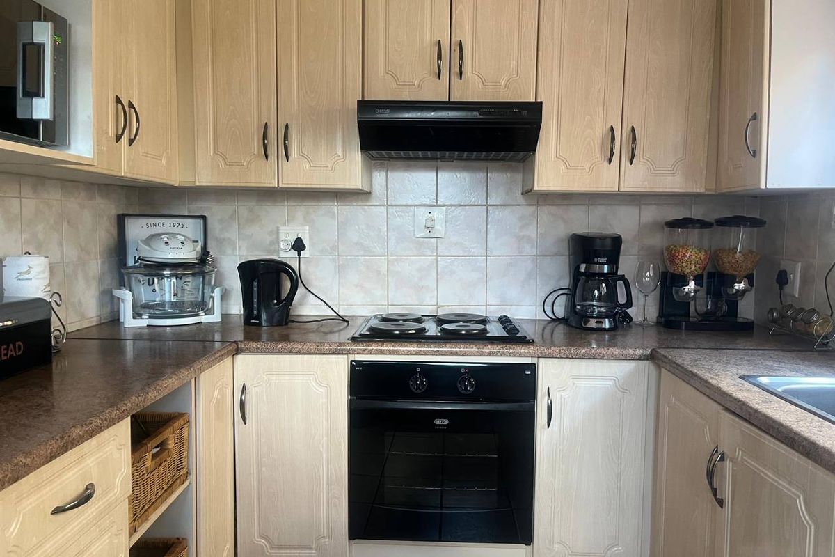 A functional kitchen featuring light wood-finish cabinetry, laminate countertops, a tiled backsplash, and integrated appliances including an oven, hob, and extractor fan.