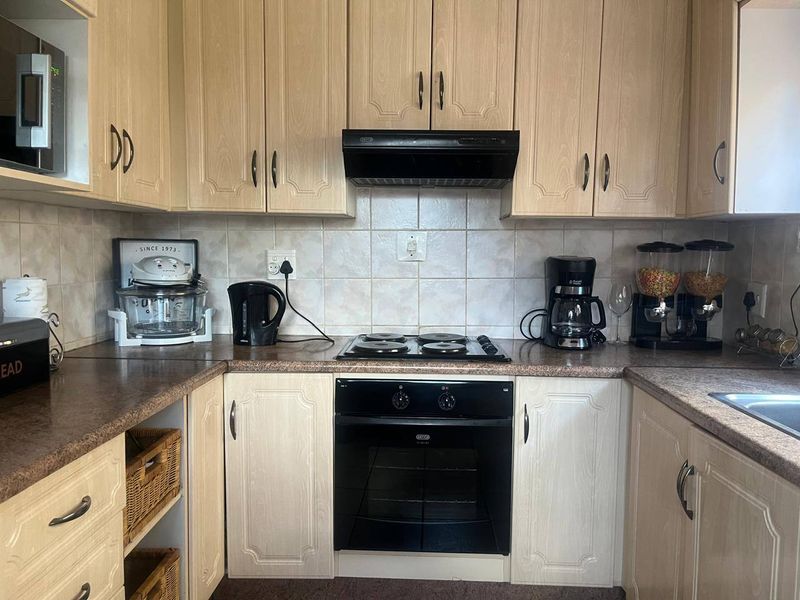 A functional kitchen featuring light wood-finish cabinetry, laminate countertops, a tiled backsplash, and integrated appliances including an oven, hob, and extractor fan.