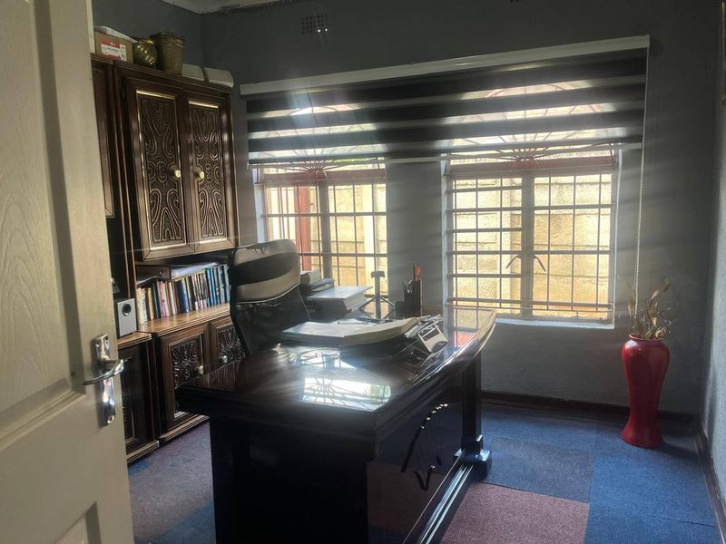 A functional home office featuring built-in wooden cabinetry, security bars on windows, and roller blinds.
