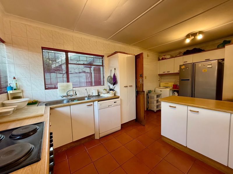 A functional kitchen featuring built-in cabinetry, tiled splashbacks, double bowl sink, and ceramic tile flooring, offering a practical layout for daily meal preparation.
