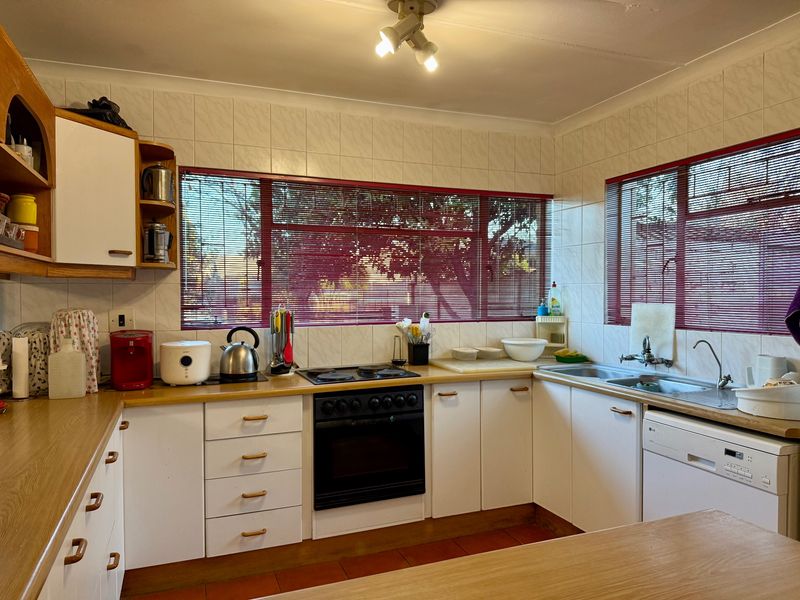 Functional kitchen featuring white cabinetry, laminate countertops, tiled splashbacks, and integrated cooking appliances with ample natural light from large windows.