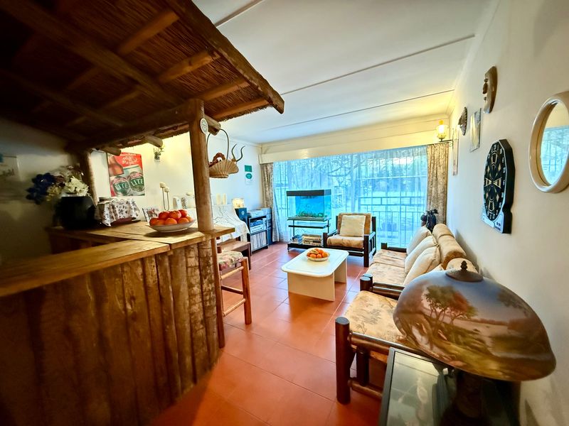 A living room featuring a built-in rustic bar with a thatched canopy, tiled flooring, and a large sliding glass door providing natural light.