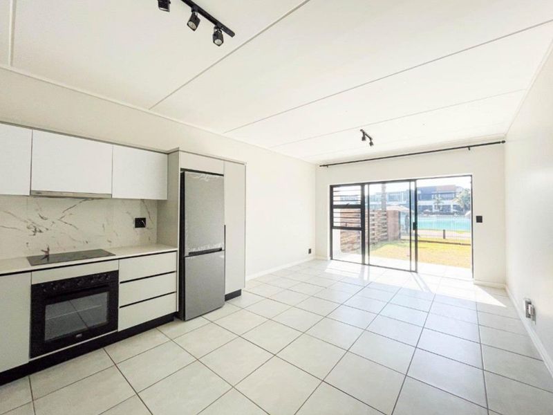 Modern open-plan kitchen and living area featuring sleek cabinetry, integrated appliances, tiled flooring, and large sliding doors leading to a private outdoor space.