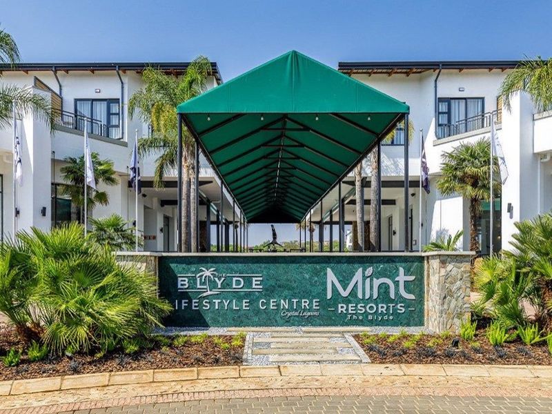 The front entrance of The Blyde Lifestyle Centre, featuring a prominent green canopy, stone-clad signage, and well-maintained landscaping.