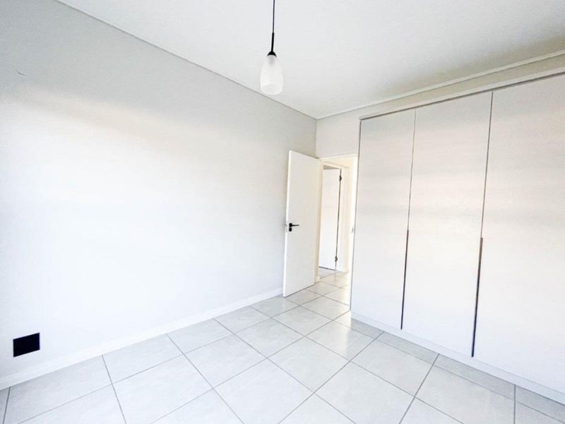 A bright, empty bedroom featuring neutral tiled flooring, a modern built-in wardrobe, and a simple pendant light fixture.