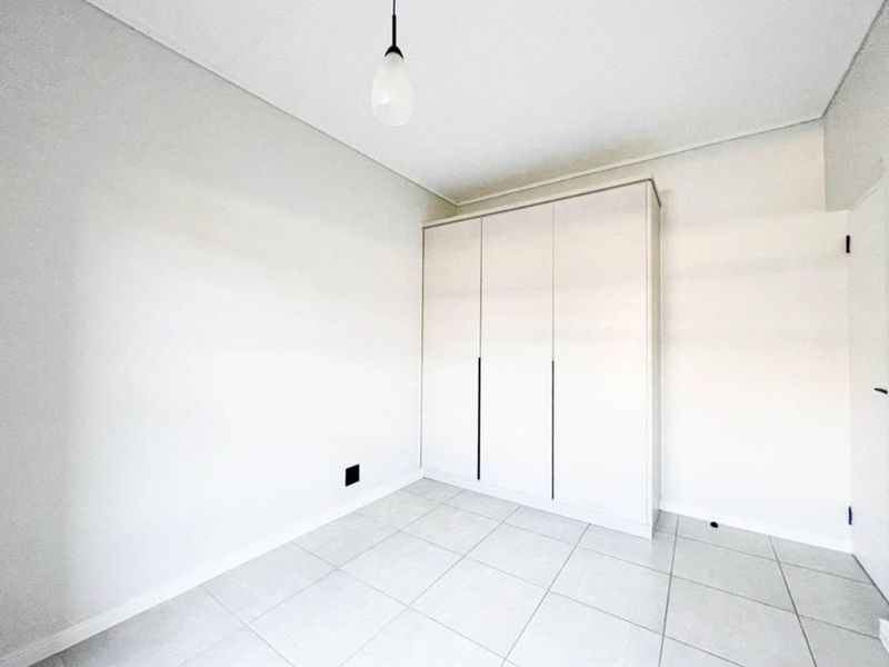 A clean, empty bedroom featuring neutral tiled flooring, a modern built-in wardrobe, and a simple pendant light fixture.