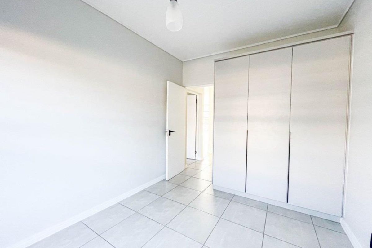 A bright, empty bedroom featuring neutral tiled flooring and a large built-in wardrobe with clean, modern finishes.