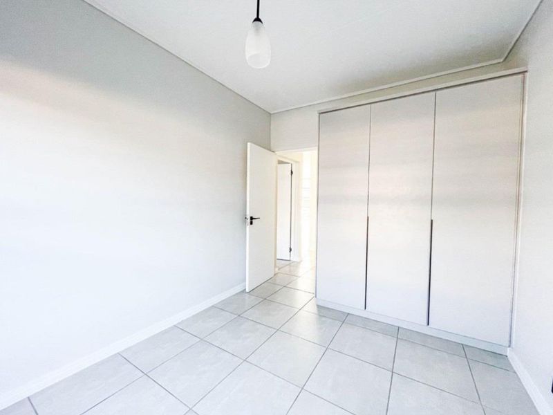 A bright, empty bedroom featuring neutral tiled flooring and a large built-in wardrobe with clean, modern finishes.