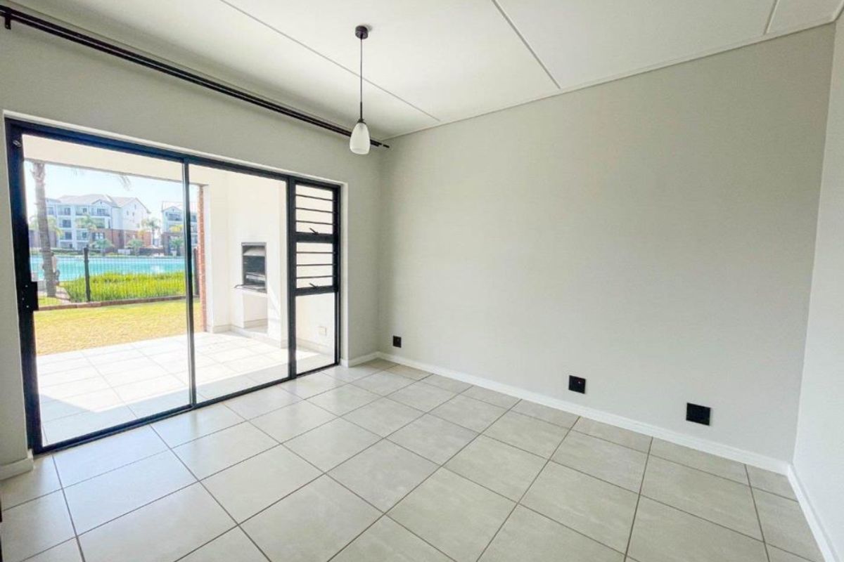 A bright, empty living area featuring neutral tiled flooring and a large sliding glass door providing access to an outdoor patio space.