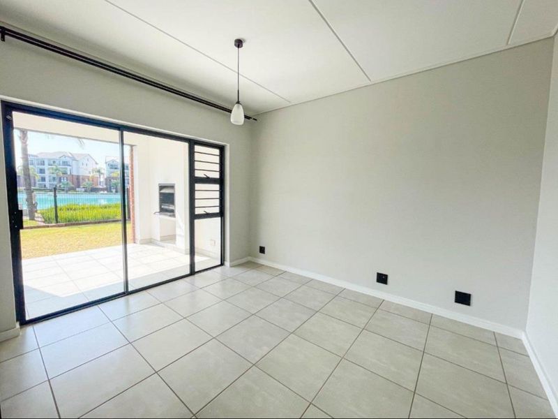A bright, empty living area featuring neutral tiled flooring and a large sliding glass door providing access to an outdoor patio space.