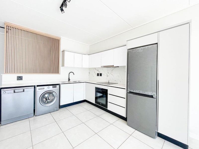 Modern, well-appointed kitchen featuring sleek white cabinetry, marble-look splashback, integrated appliances, and clean tiled flooring in a bright, contemporary space.
