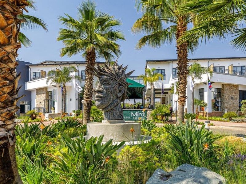 A well-maintained front exterior view of the apartment complex featuring landscaped gardens, palm trees, and modern architectural stone and white facade finishes.