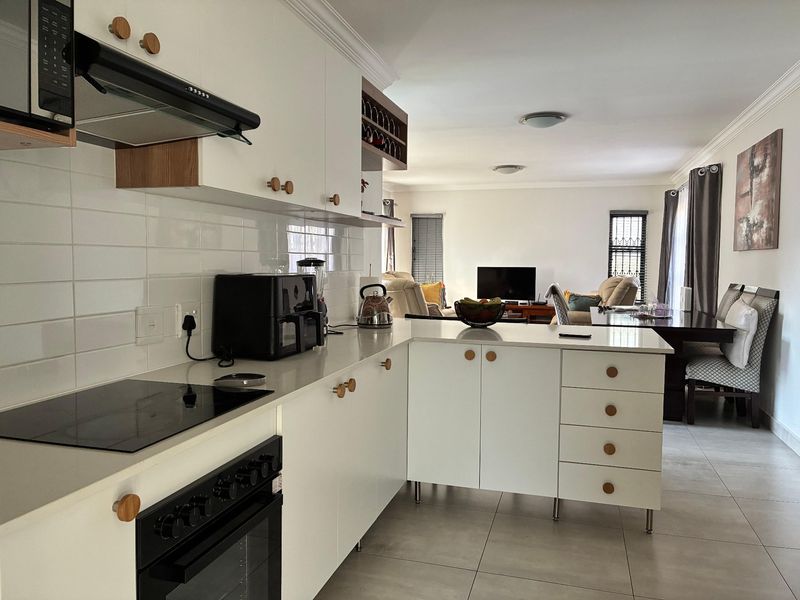 Modern open-plan kitchen featuring white cabinetry, quartz countertops, subway tile backsplash, and integrated appliances, flowing seamlessly into the dining and living area.